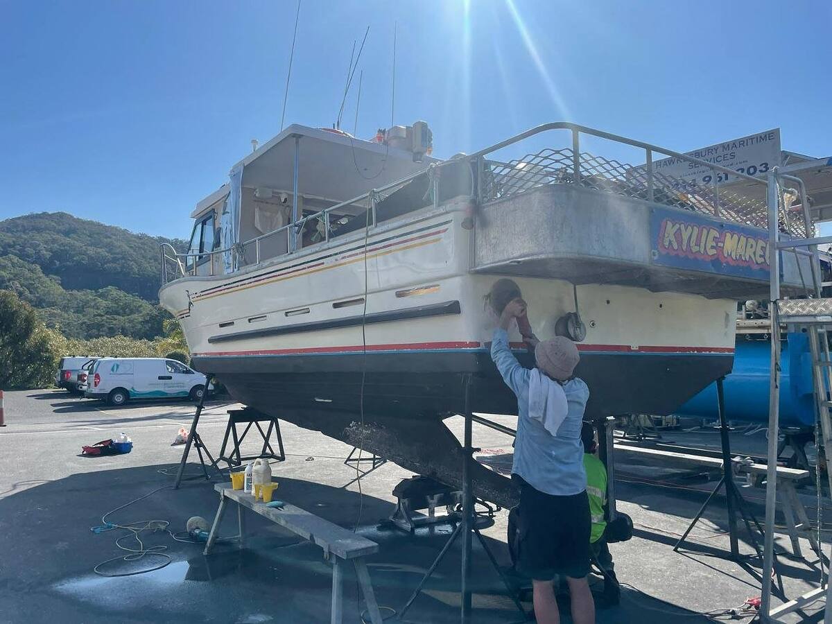 Detailer polishing the hull of a cruiser on stands at the boatyard