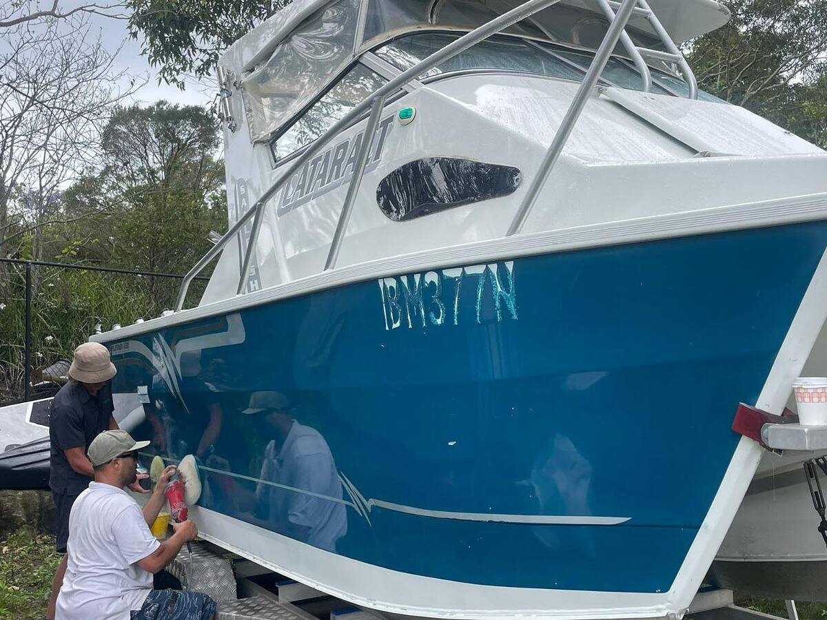 Two detailers machine polishing the blue hull of a trailer boat