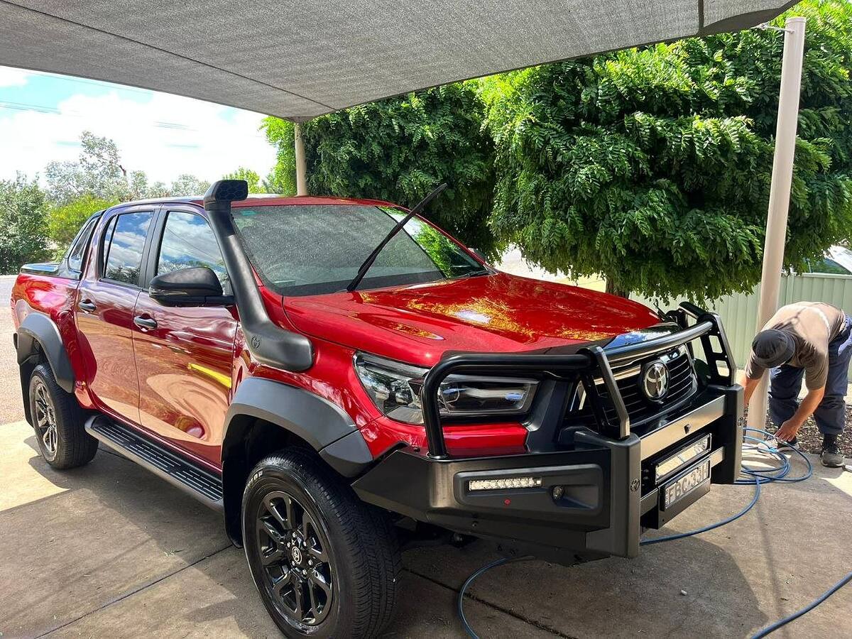 Red Toyota HiLux gleaming after a mobile car detail, detailer packing up the hose