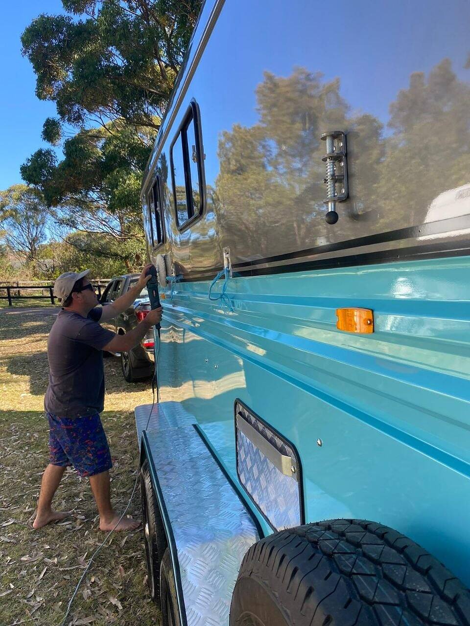 Detailer machine polishing the side of a blue off-road caravan