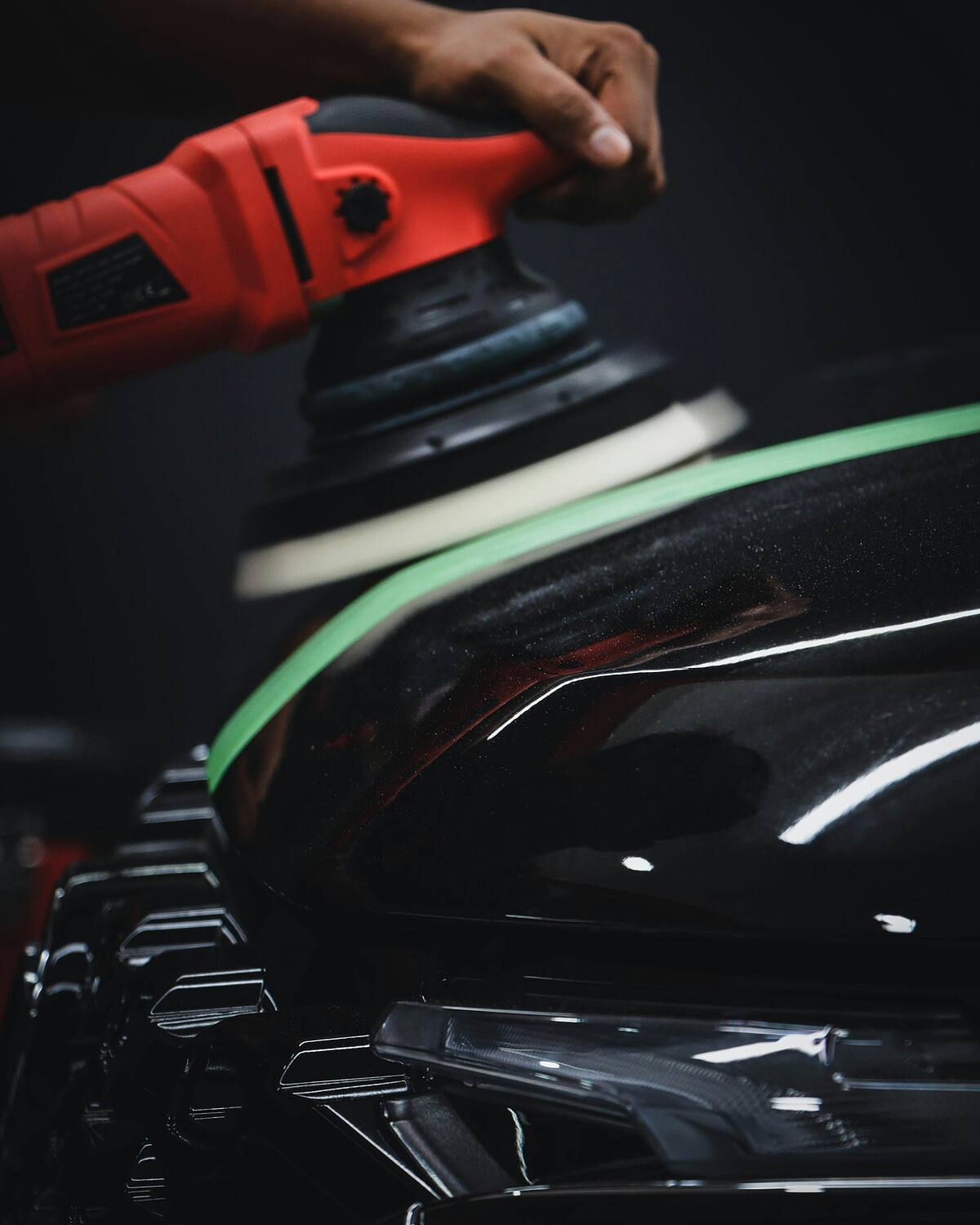 Dual-action machine polisher with a foam pad on glossy black paint